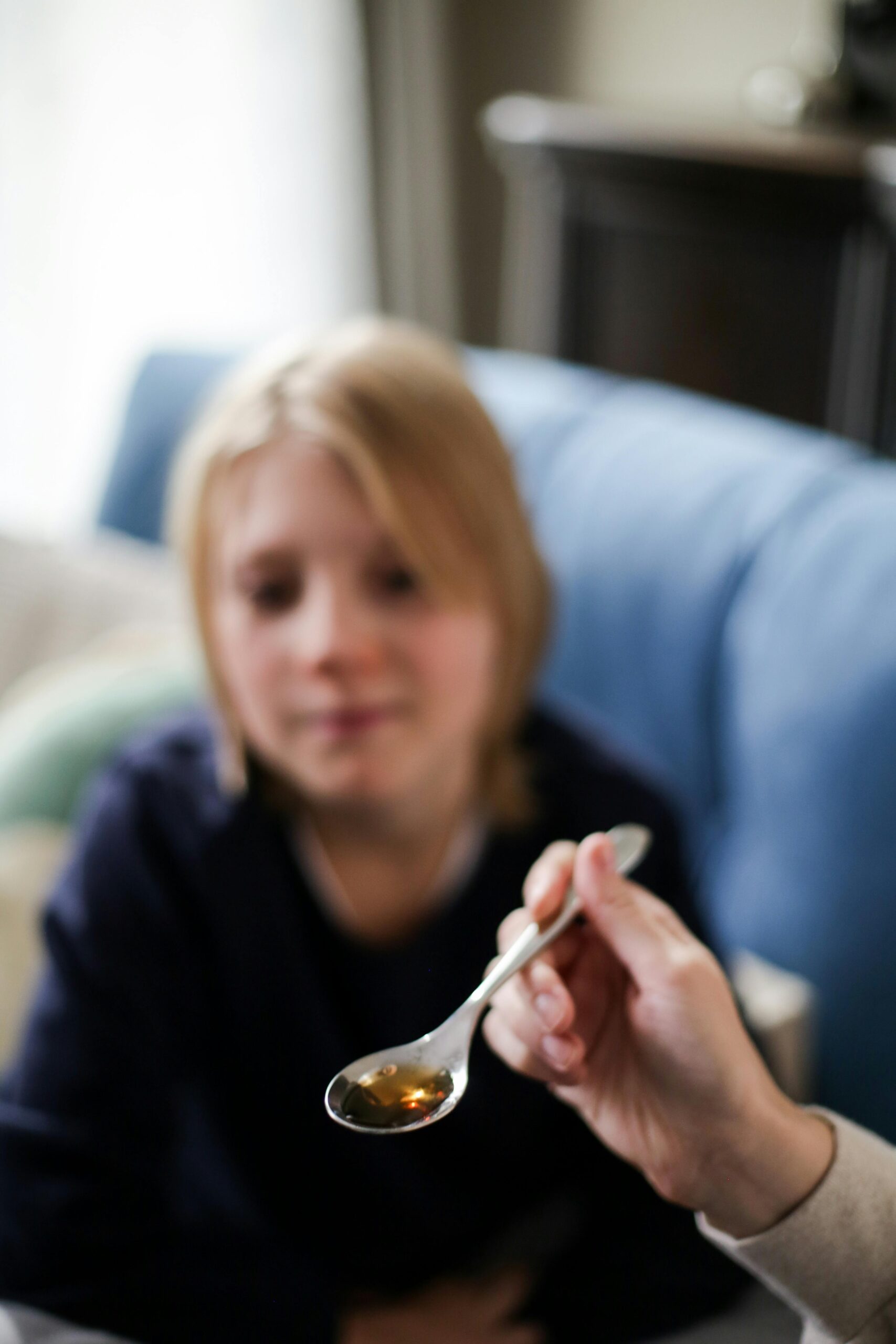 Out of focus child ready to take liquid medicine from a spoon.